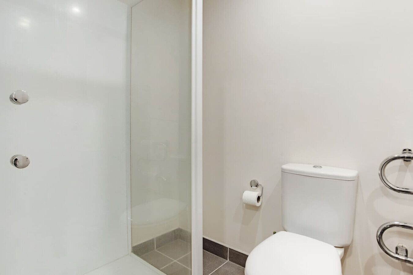 Een moderne badkamer met een douchecabine van glas, een toilet en een handgreep.