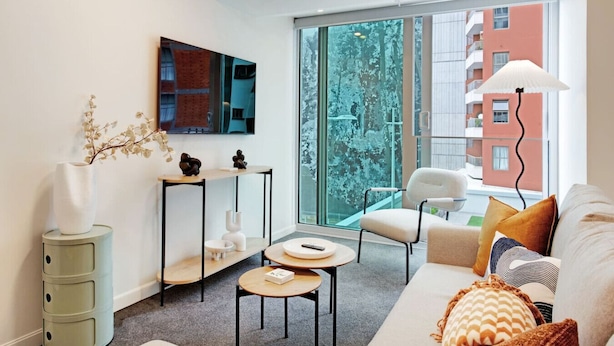 Una sala de estar moderna con un ventanal grande, un sofá, una mesa de centro, un televisor y una mesita auxiliar.