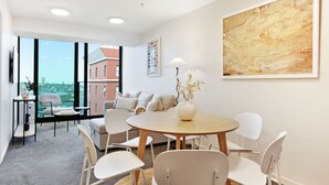 Un salon moderne avec une table ronde en bois, des chaises blanches, un canapé et un grand tableau abstrait accroché au mur.