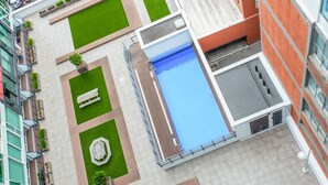Une piscine sur le toit, avec un élément décoratif aquatique aux eaux bleues, entourée de pelouses verdoyantes et d’espaces aménagés pour se détendre.