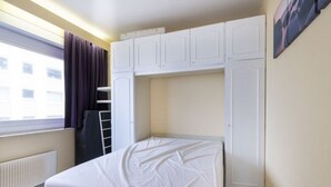 A small, single-bed room with a window, a radiator, and a wardrobe.