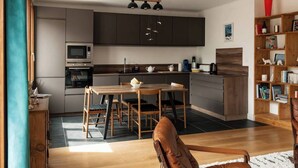A modern kitchen with dark cabinets, a wooden dining table, and a coffee machine. - Welcome to Annecy!<br>Enjoy a comfortable stay in our bright apartment, located in a quiet residential area. Just a 10-minute walk from the train station and the historic center, and 20 minutes from the lake — the perfect location to explore the city (Sévrier)