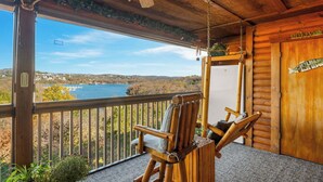 A wooden cabin with a balcony overlooking a lake, a wooden chair, and a refrigerator.