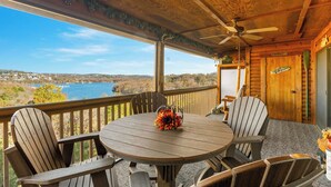 A wooden deck with a round table and chairs, overlooking a lake and distant landscape.