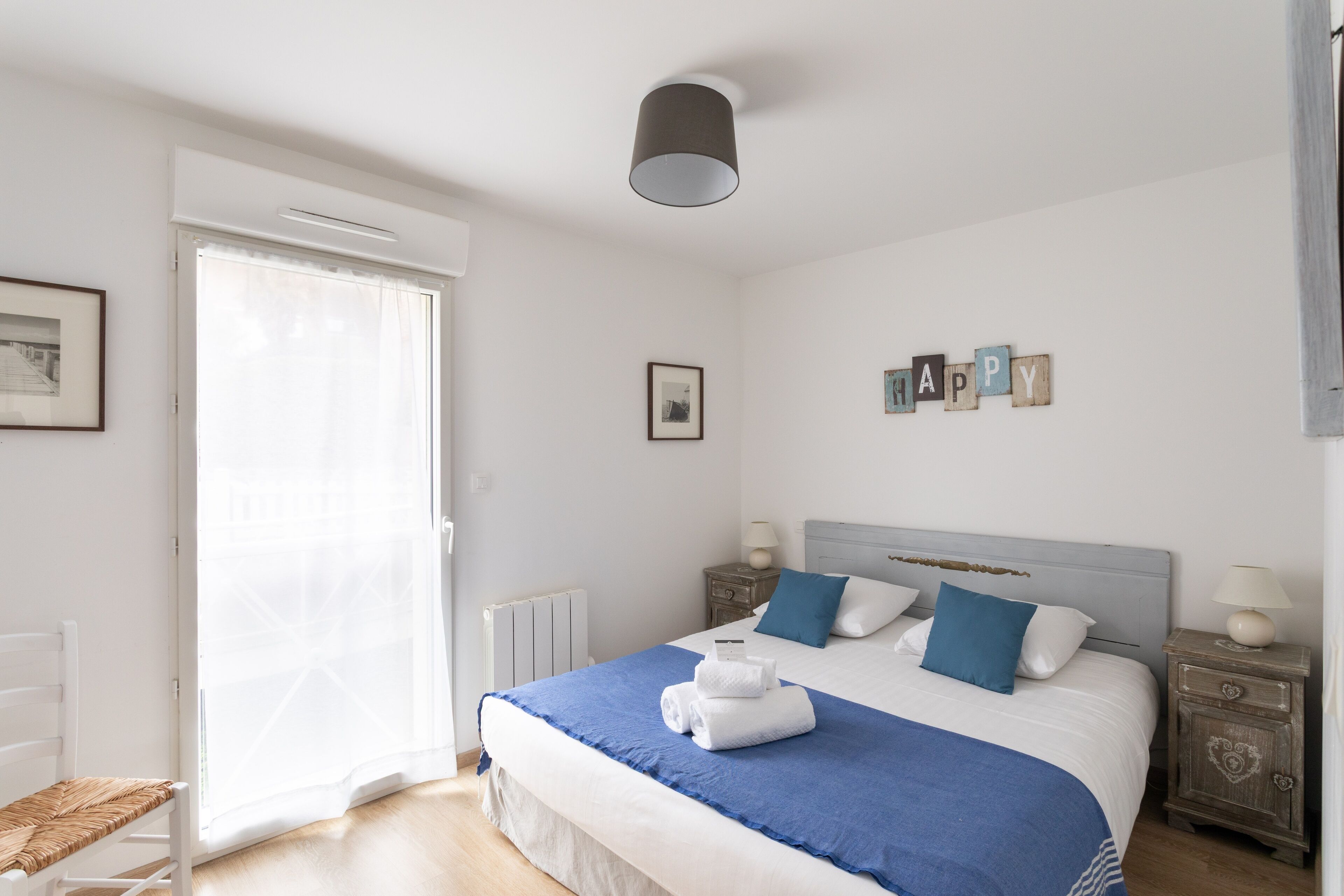 Een netjes ingerichte slaapkamer met een bed, nachtkastjes, een stoel en een raam met gordijnen.