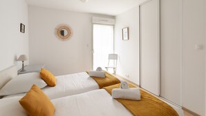 Ein Hotelzimmer mit zwei Betten, einem Sessel, einer Lampe und einem großen Spiegel.