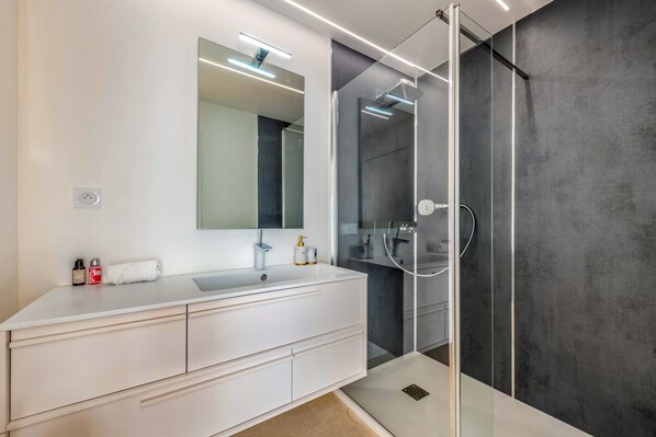 Une salle de bain moderne avec un meuble-lavabo blanc, un grand miroir et une douche séparée par des parois en verre.