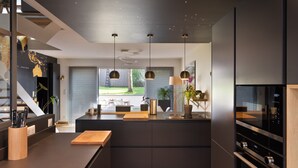 Eine moderne Küche mit einer zentralen Kochinsel, Pendelleuchten und einem großen Kühlschrank.