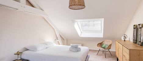 A bedroom with a bed, a side table, a chair, a wooden dresser, and a hanging light fixture.