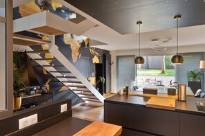 Una cocina moderna con una isla central, una escalera con un mapa mundial e iluminación colgante.