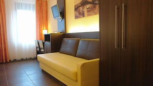 A yellow sofa, a television mounted on the wall, and a wooden cabinet. - San Remo Fine.Food.Hotel (Nuremberg)