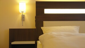 A hotel room with a neatly made bed, a bedside table, and a wall-mounted light fixture. - San Remo Fine.Food.Hotel (Nuremberg)