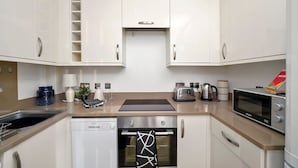 Uma cozinha moderna com armários brancos, lava-louças, forno, micro-ondas e torradeira.
