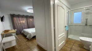 Un dormitorio con cama, escritorio y silla. Incluye un baño con inodoro, ducha y ventana.