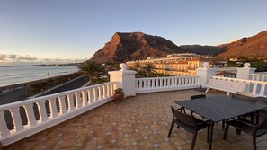 Una terraza con vistas al mar y a las montañas, con una mesa y sillas.