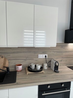 A modern kitchen with white cabinets, a wooden countertop, a coffee maker, a toaster, and a cutting board. - Seaside cottage (Luc-sur-Mer)