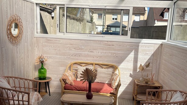 A sunlit room with a glass ceiling, wicker furniture, a red sofa, and a view of neighboring buildings.