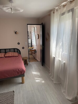 A bedroom with a bed, a ceiling fan, a door leading to a bathroom, and sheer curtains.
