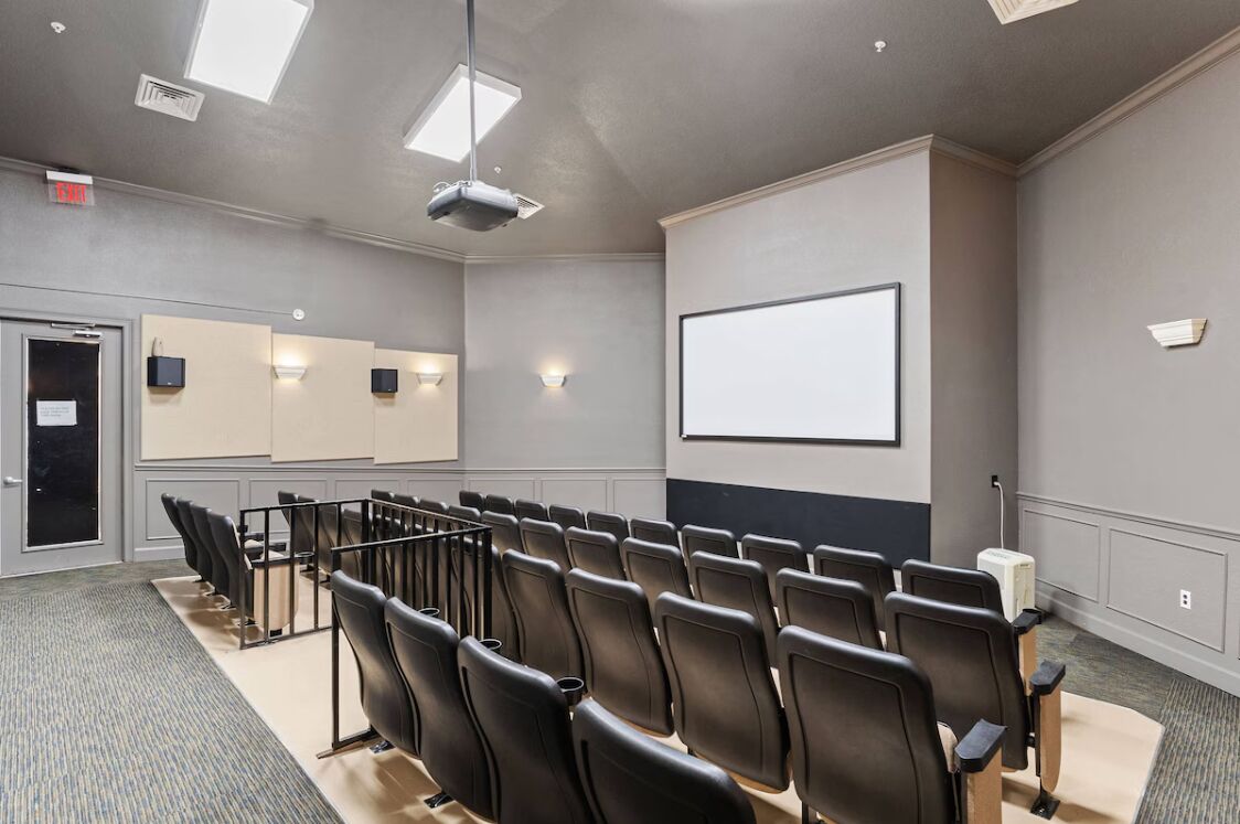 A conference room with rows of chairs, a projector, a screen, and a door.