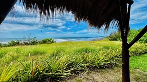 A beach view with a thatched roof structure, green grass, and a clear sky.