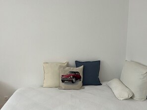 A bed with a white textured bedspread and four pillows in different colors and designs.