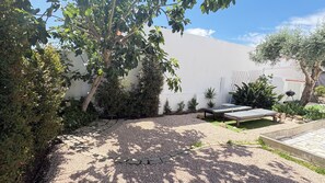 Une cour avec un espace aménagé pour s’asseoir, un mur blanc et diverses plantes.