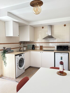 A compact kitchen with a washing machine, a microwave, and a small refrigerator.