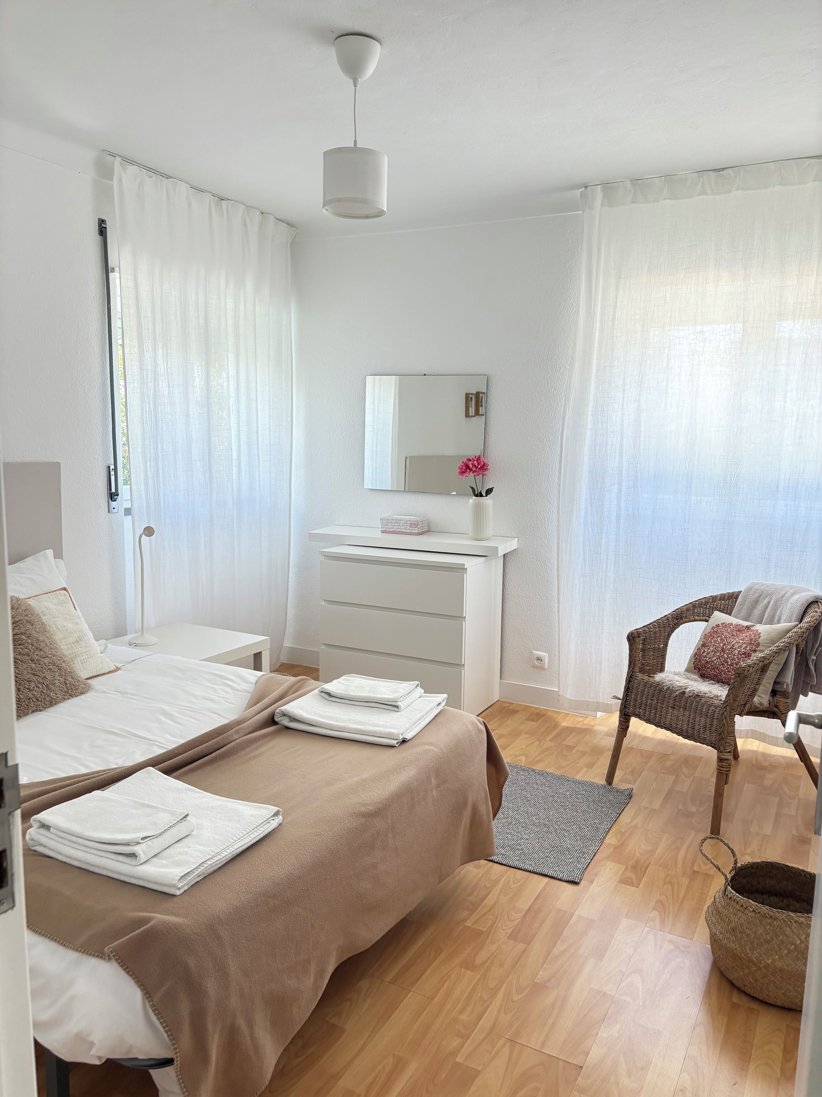A hotel room with a bed, a desk, a chair, a mirror, and a hanging light fixture.