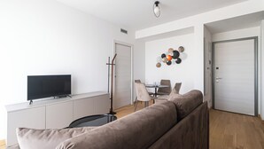 A modern living room with a flat-screen TV, a sofa, a dining table with chairs, and a decorative wall piece. - Italianway Comfort - Pasolini 70 C - Feel Uptown (Milano)