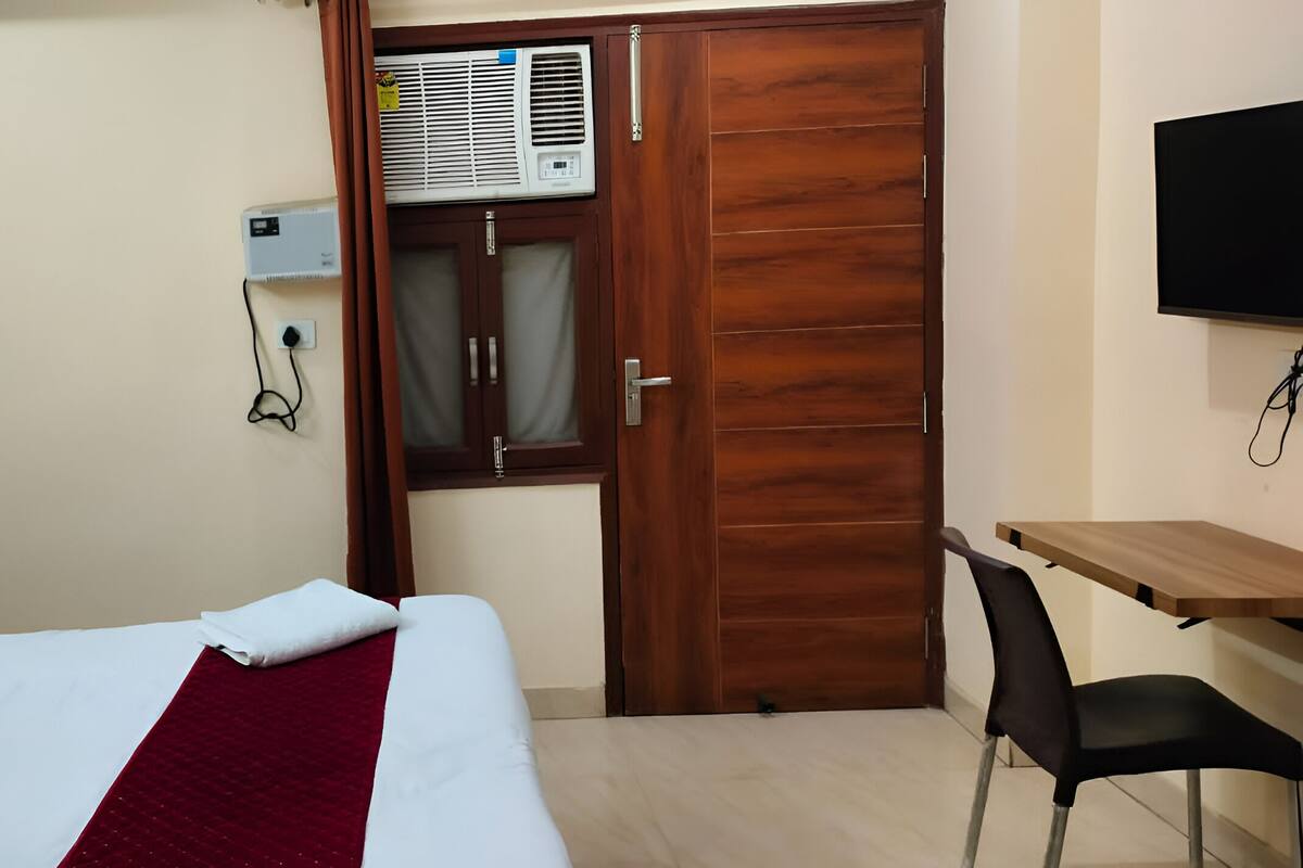 Ein Hotelzimmer mit Bett, Schreibtisch, Stuhl, Klimaanlage und Fernseher.