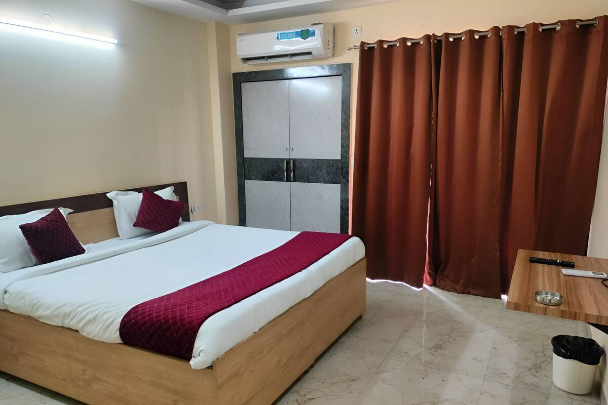 Ein Hotelzimmer mit Bett, Schrank, Vorhang, Nachttisch und Mülleimer.