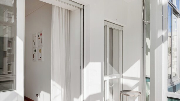 A bright, modern room with a sliding glass door leading to a balcony, a small round table, and a view of a pool. - Luz & Mar at Coastal Oeiras (Oeiras)