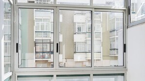 A bright room with large windows, a woven rug, and a view of a building with balconies. - Luz & Mar at Coastal Oeiras (Oeiras)