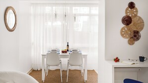 A dining area with a white table set for four, a mirror on the wall, and decorative wall art. - Luz & Mar at Coastal Oeiras (Oeiras)