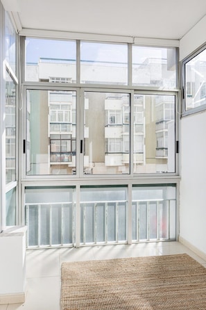 A room with large windows, a woven rug, and a view of a building with balconies. - Luz & Mar at Coastal Oeiras (Oeiras)