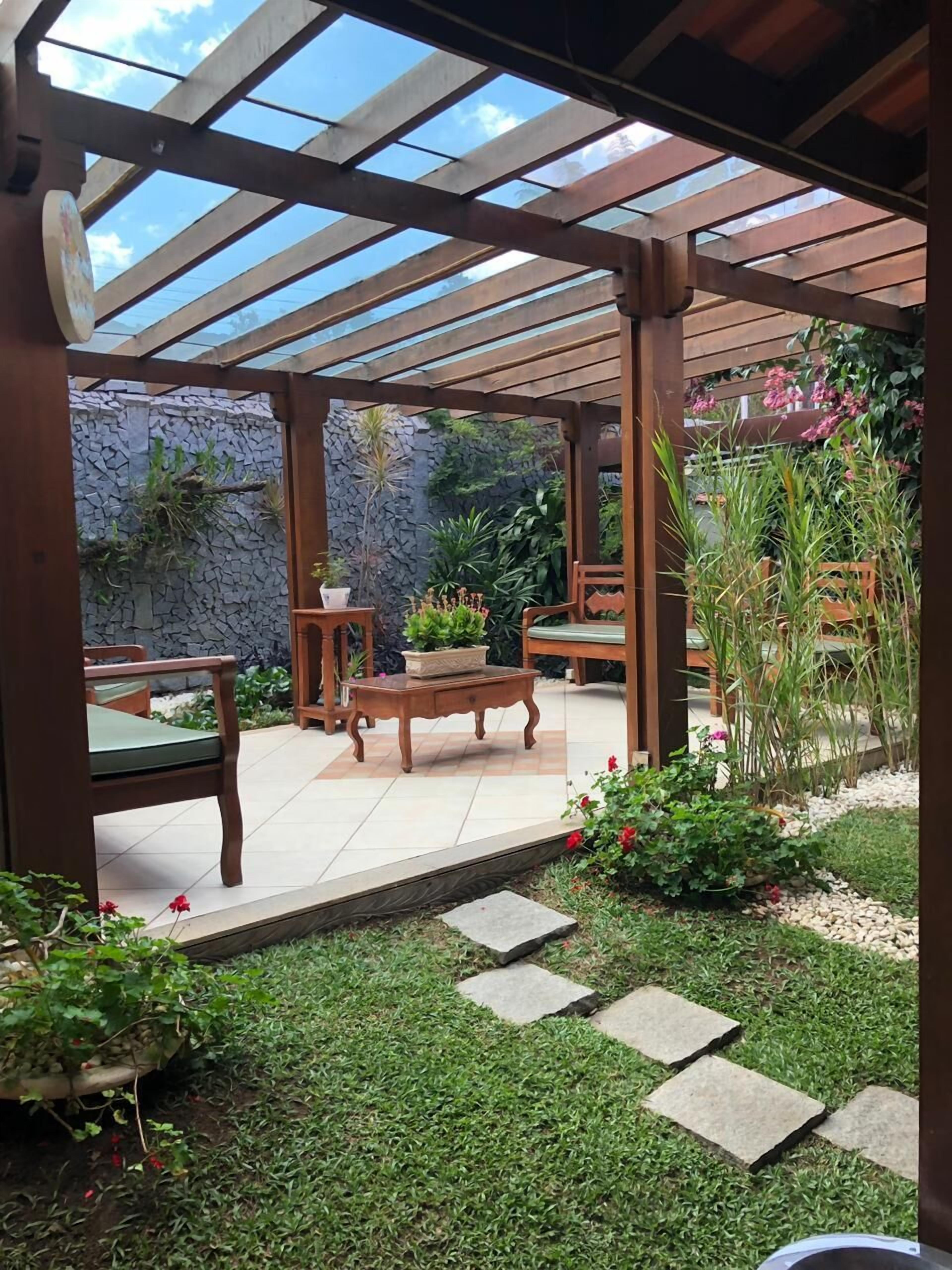 A covered patio area with wooden furniture, a stone wall, and potted plants.