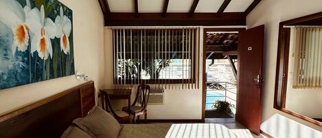 Un dormitorio con cama, escritorio, silla, un cuadro, ventilador de techo y vistas al exterior.
