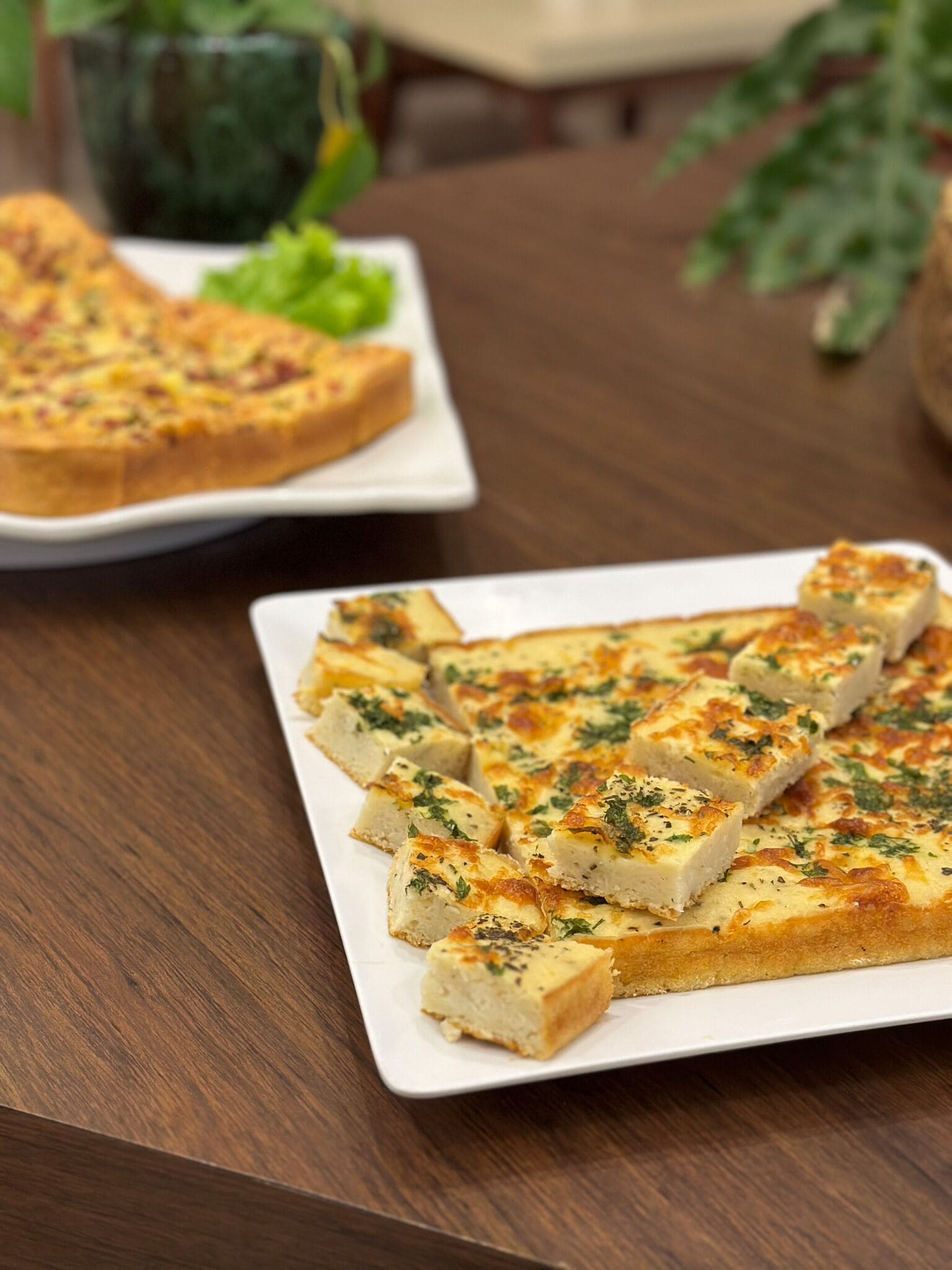 Un plato blanco rectangular con varios trozos cuadrados de comida horneada, probablemente queso o pan, adornado con hierbas.