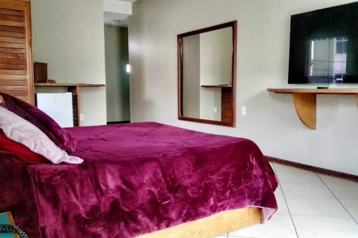 A room with a bed, a television on a stand, a mirror, and a desk.