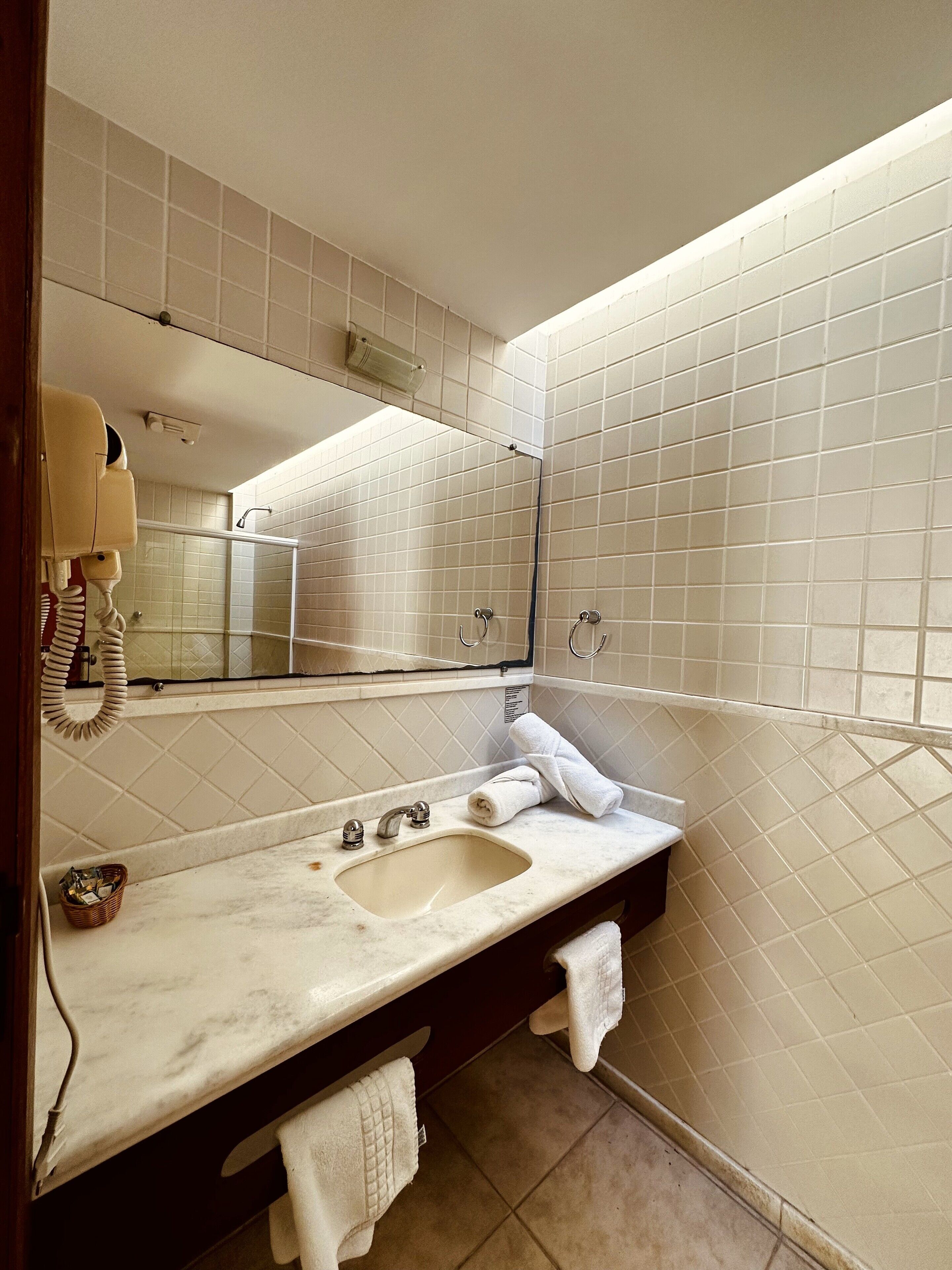 A bathroom with a marble sink, a mirror, a towel rack, and a hand dryer.