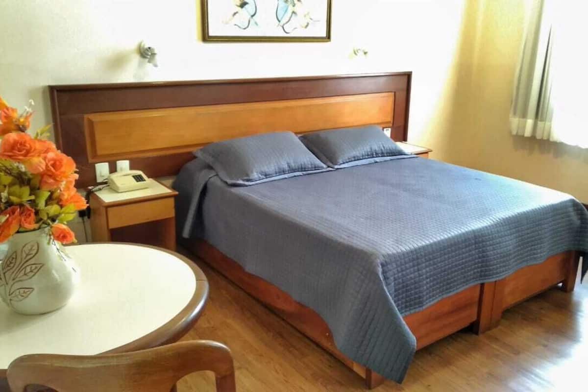 A bedroom with a wooden bed, a bedside table with a phone, a vase with flowers, and a round table.