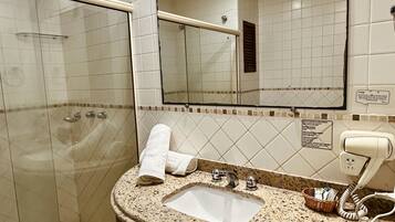 A bathroom with a glass-enclosed shower, a sink with a mirror above it, and a hairdryer on the countertop.