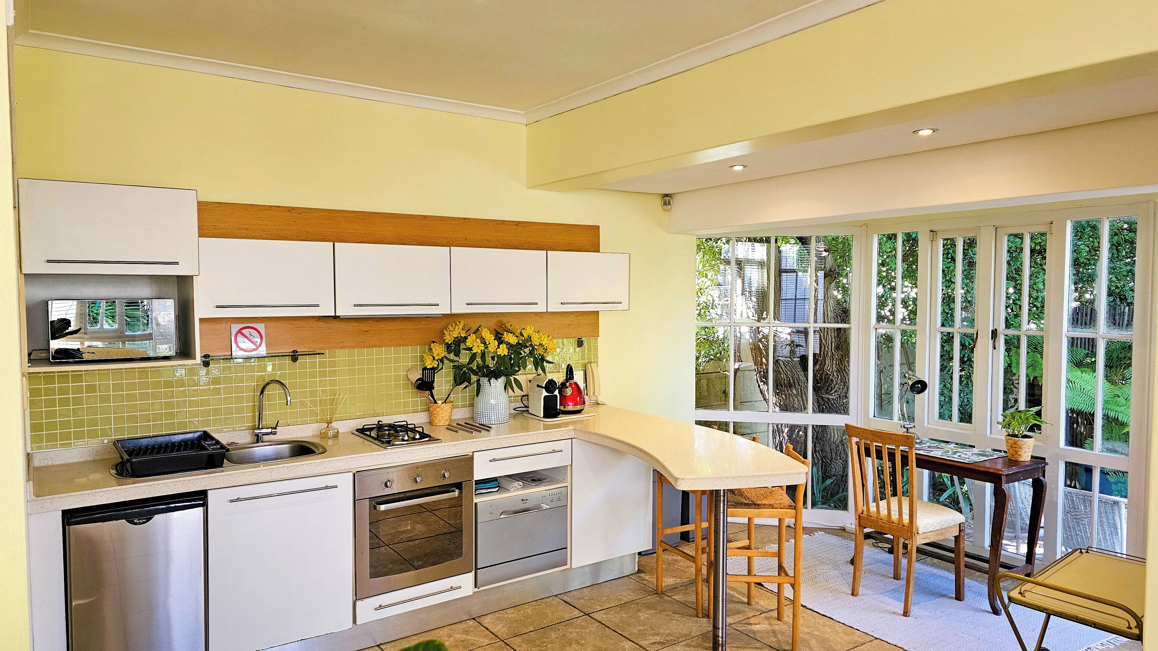 A kitchen with white cabinets, a sink, a stove, and a dining area with a table and chairs.