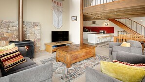 Ein großzügiges Wohnzimmer mit Kamin aus Stein, einem Holztisch und einem grauen Sofa.