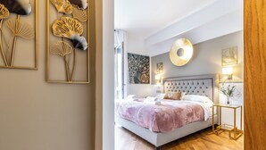 Une chambre à coucher moderne avec un grand lit, une tête de lit capitonnée et une table de chevet avec une lampe.