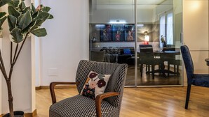 Un salon moderne avec un fauteuil à motifs, une cloison en verre et un coin repas visible à travers la cloison.