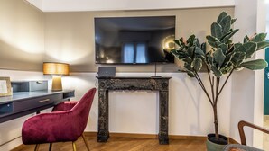 Un salon moderne avec un téléviseur à écran plat fixé au mur, une table basse en bois foncé, un fauteuil en velours rouge, une plante en pot et un plancher en bois.