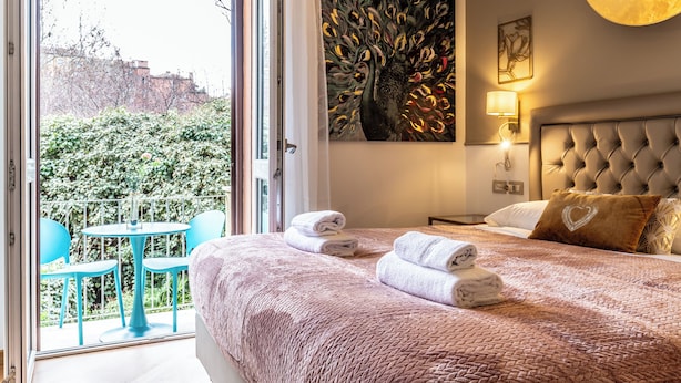 Une chambre d’hôtel avec un lit, un tableau, un balcon avec des chaises et une vue sur la verdure.