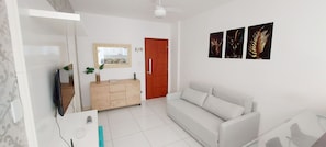 A modern living room with a white sofa, a wooden cabinet, a TV, and a mirror. - COOND0100 - Edifício Solarius (Salvador)