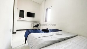Camera da letto con un letto, una TV a parete, una finestra con tende e una sedia.